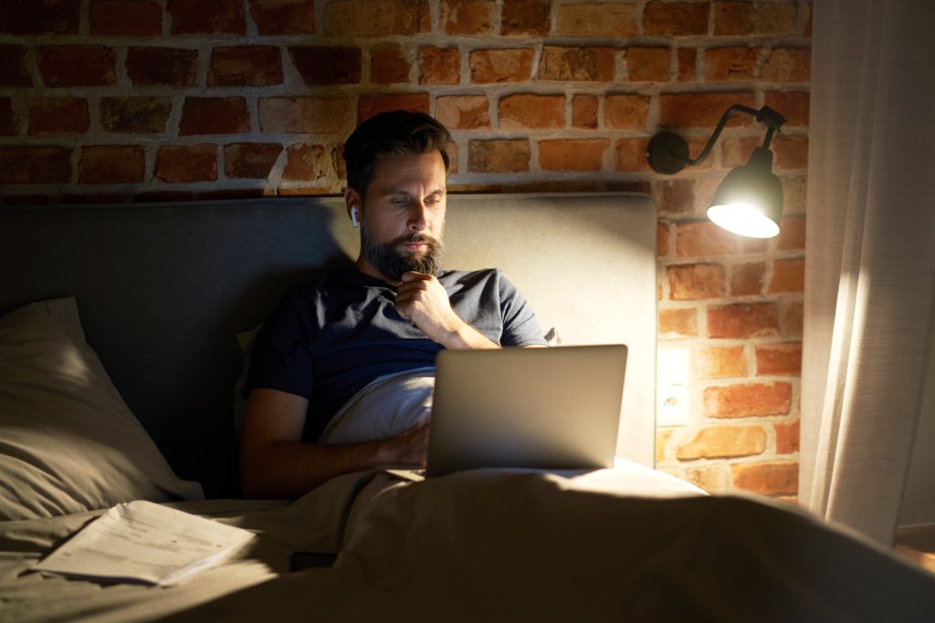 Man working on laptop from bed at night